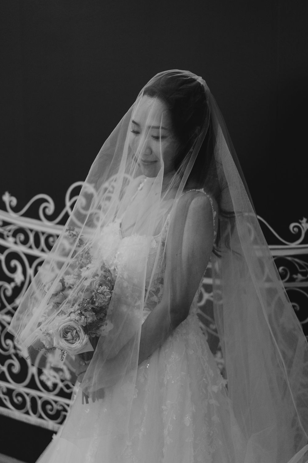 Black and white portrait of a smiling bride in a wedding dress and veil holding a bouquet.