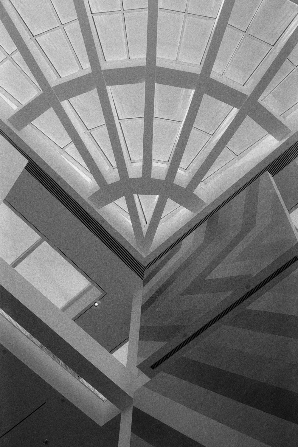 Black and white architectural photo of a fan-shaped skylight above a geometric staircase.