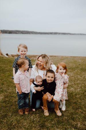 Family group sitting together on grassy hill overlooking a serene lake on an overcast day.