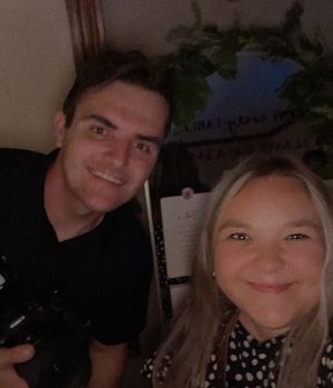 Two people taking a selfie together in an indoor setting with a houseplant visible in the background.