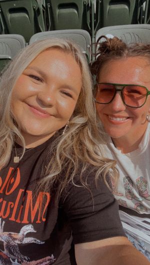 Two people sit together in stadium seats, smiling while taking a selfie-style photo.