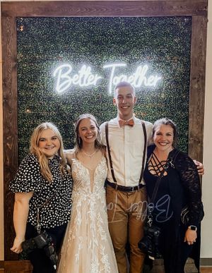 A group poses in front of a leafy wall with a glowing 'Better Together' neon sign behind them.