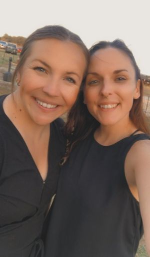 Two smiling people in black tops taking a selfie outdoors with a warm sunset glow.