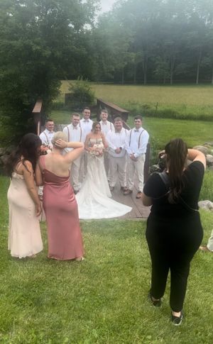 A wedding party poses outdoors on a grassy lawn while two photographers capture photos on a misty summer day.
