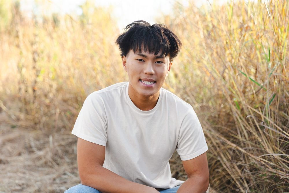 Person in white t-shirt sitting in golden field during sunset.