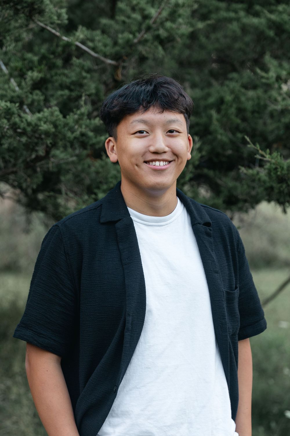 Casual portrait series of person in white t-shirt and black jacket against natural background.