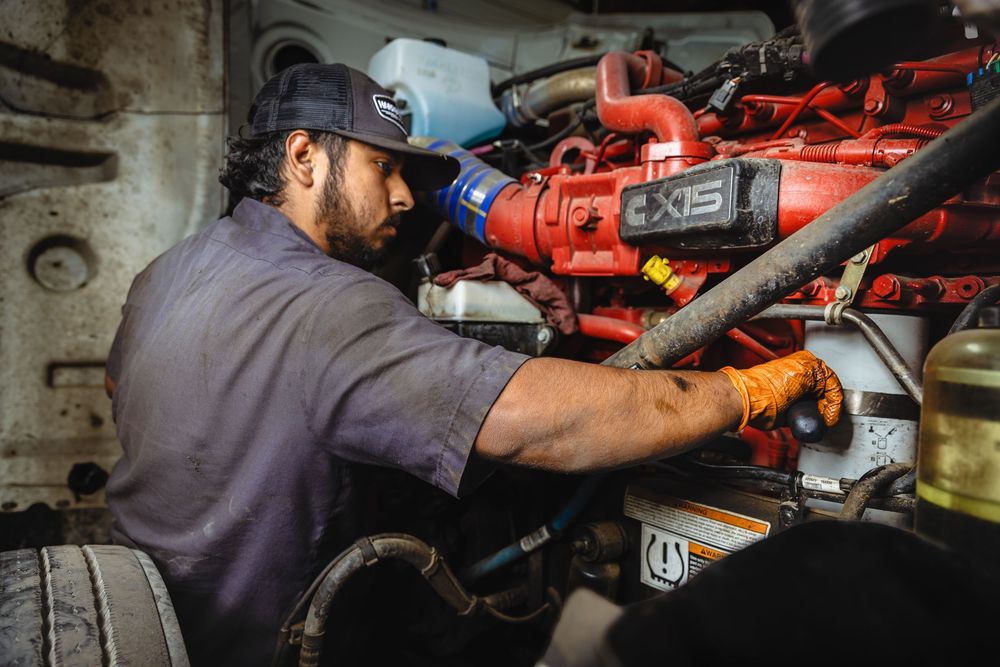 A mechanic works on a large red Cummins X15 diesel engine, wearing gloves in a tight engine compartment.