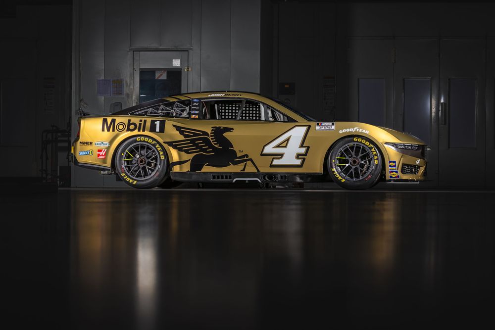 Racing cars displayed in dramatic lighting inside dark showroom or garage.
