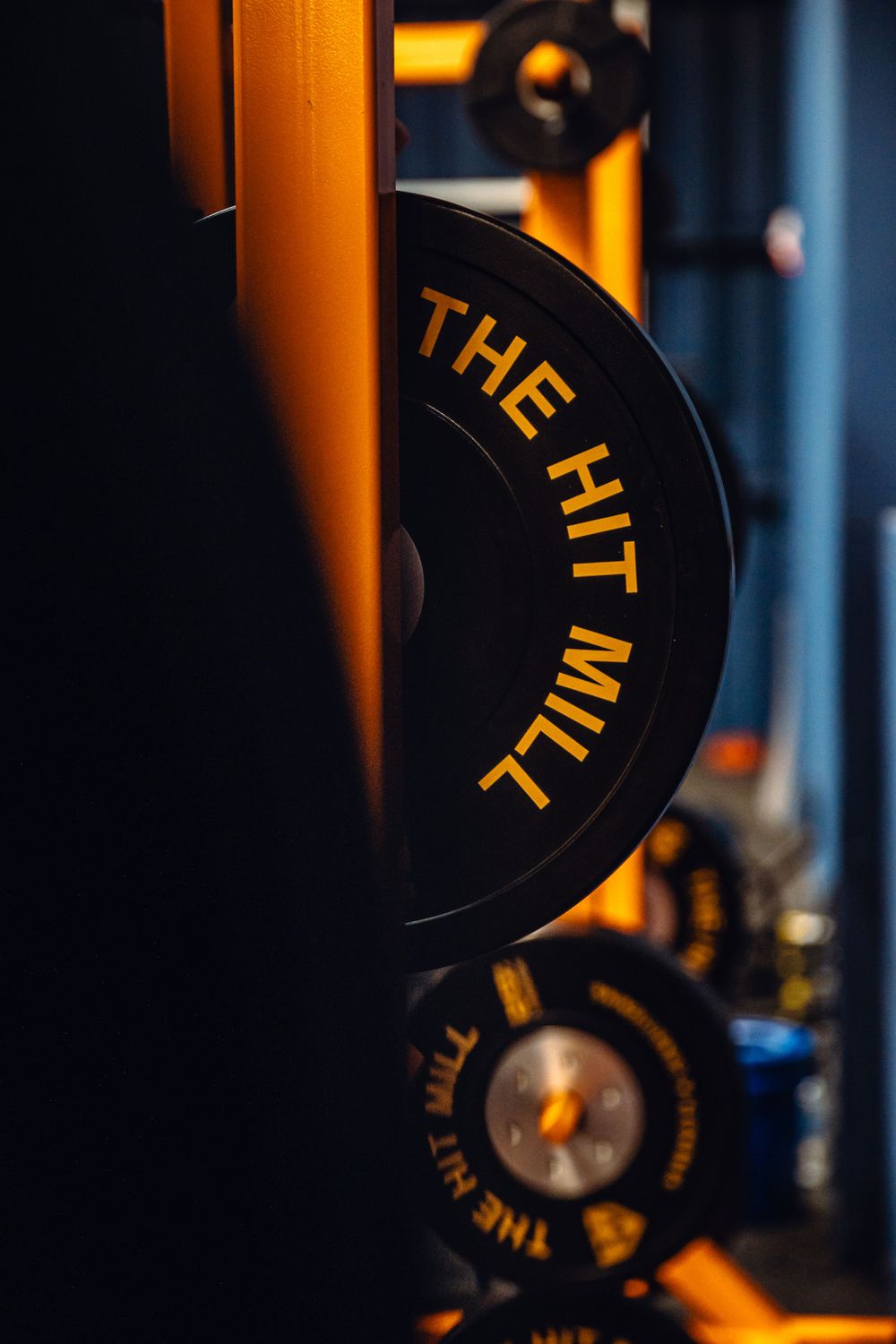 Close-up of weight plates with orange ambient lighting in dark gym environment.