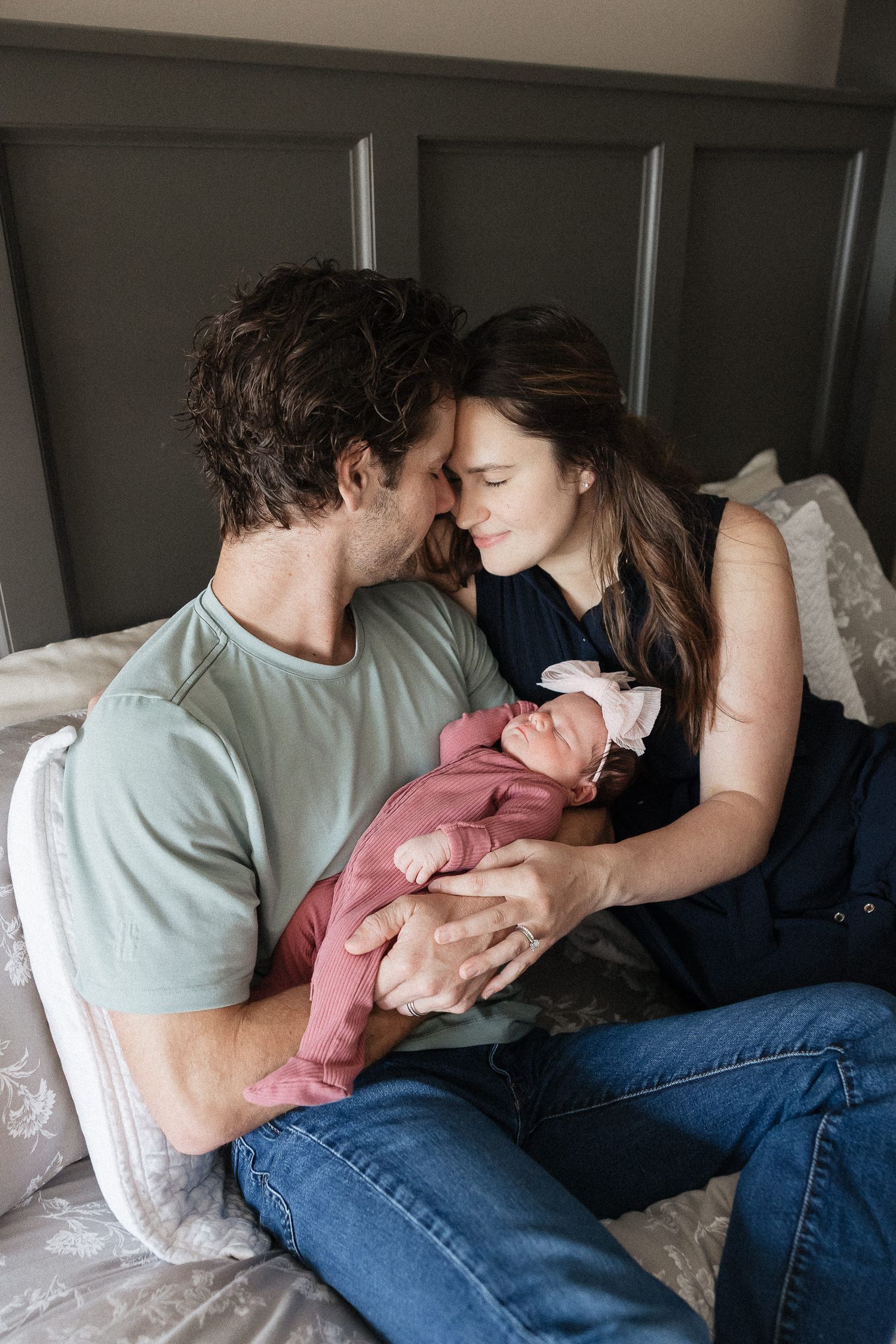 mom and dad sitting on their master bed holding sleeping newborn baby girl family photographer kansas city