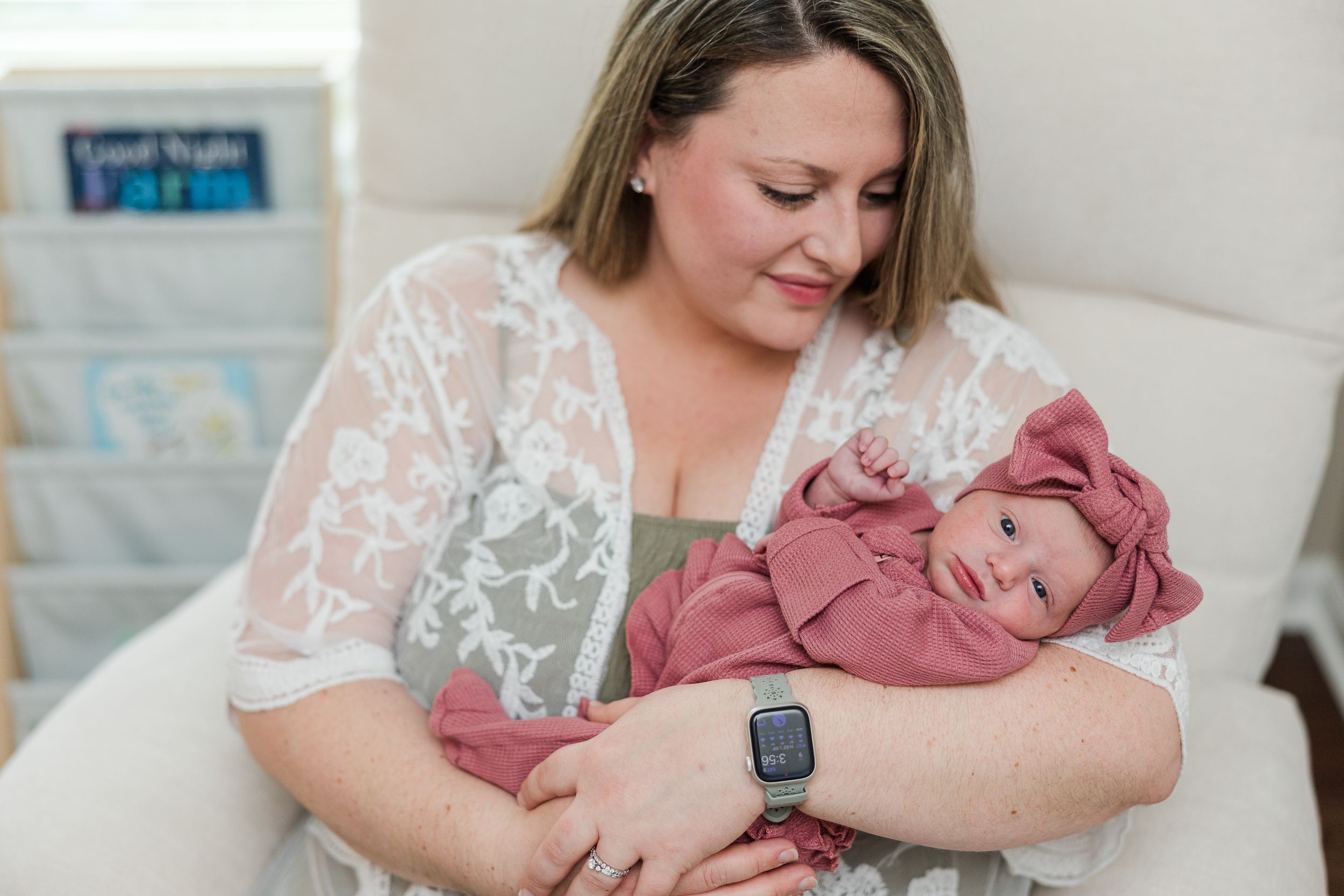 A mother tenderly holds her newborn baby wrapped in a pink swaddle while sitting in a nursery chair.