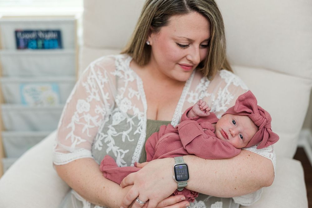 A mother tenderly holds her newborn baby wrapped in a pink swaddle while sitting in a nursery chair.