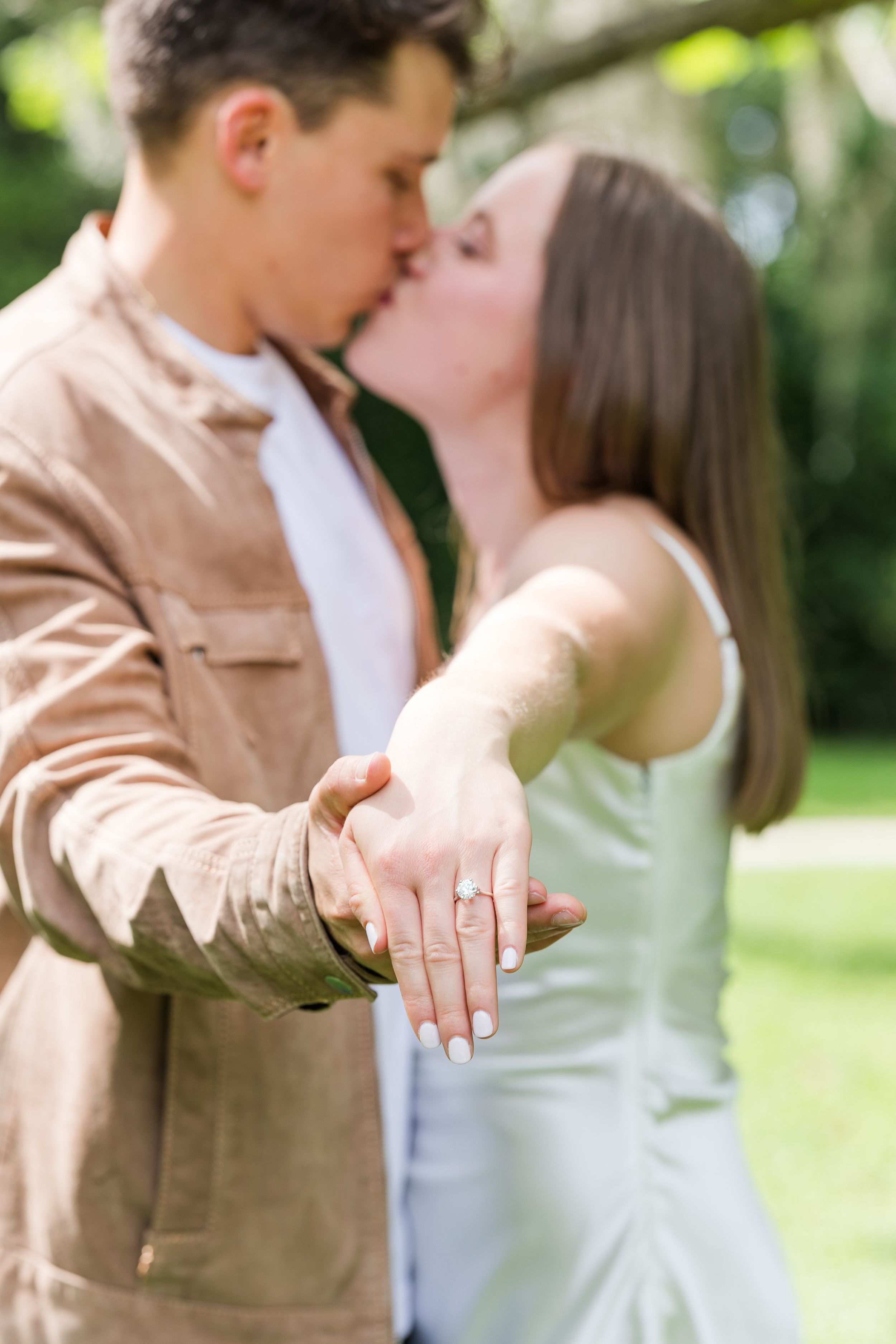 Close-up of engagement ring with couple in soft focus wearing beige and mint green.