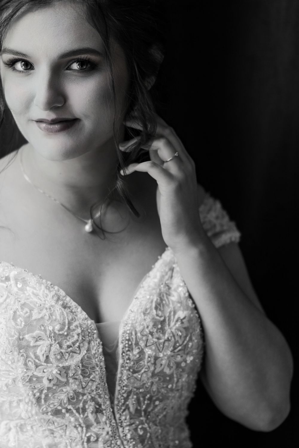 Black and white bridal portrait showing intricate lace wedding dress details and pearl jewelry.