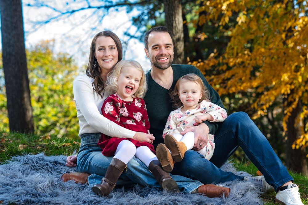 A family sits together on a rock during autumn with golden fall foliage in the background.