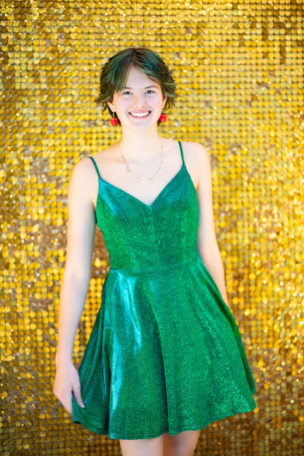 Emerald green cocktail dress sparkles against a shimmering gold sequined background.