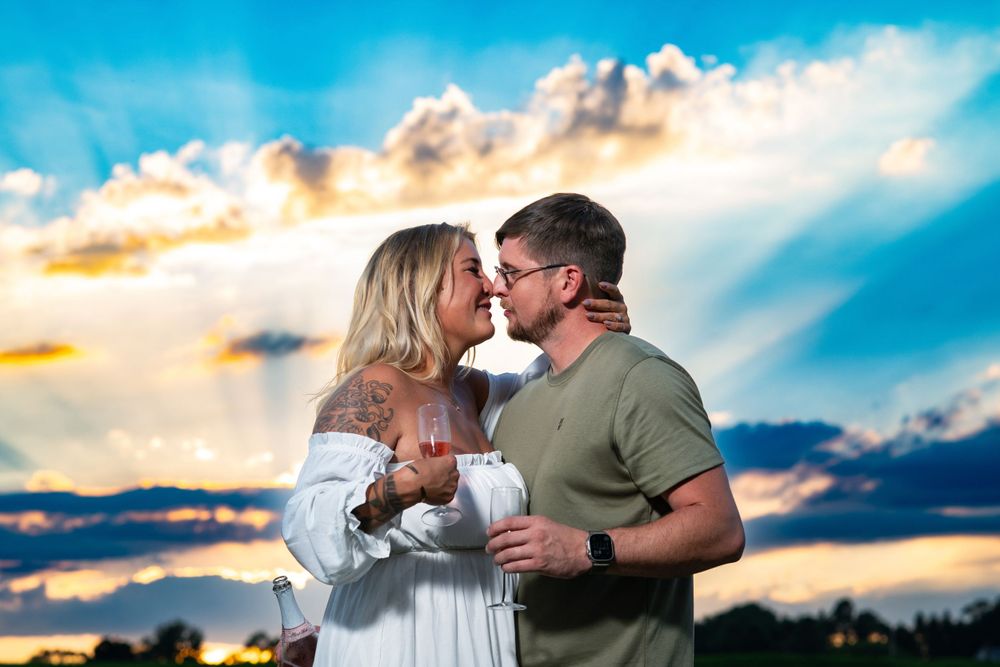 A couple shares a romantic moment at sunset with dramatic clouds and golden light in the background.