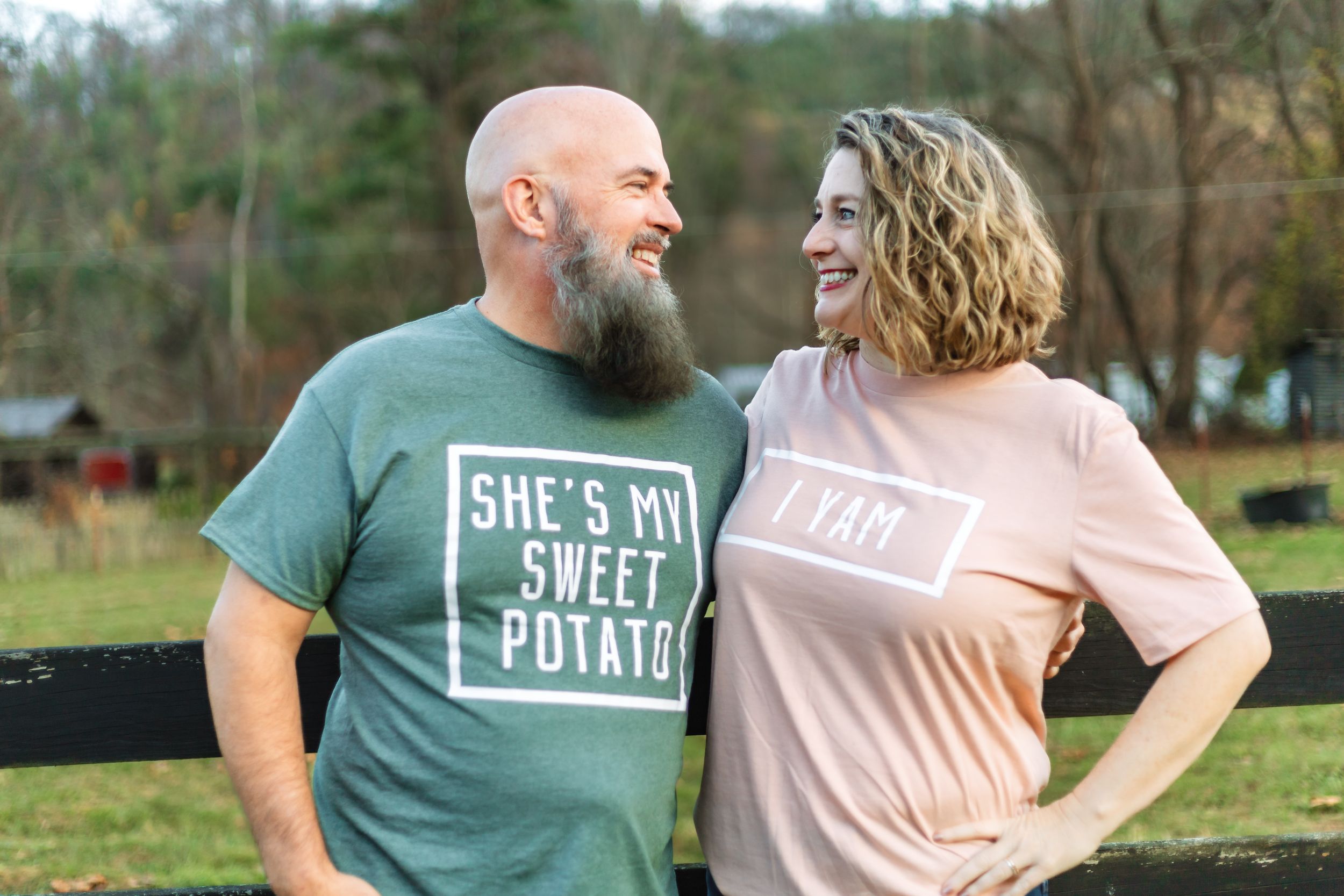 Couple sharing a laugh while wearing matching sweet potato themed shirts outdoors.