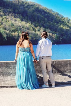A couple sits together on a concrete wall overlooking a serene mountain lake.
