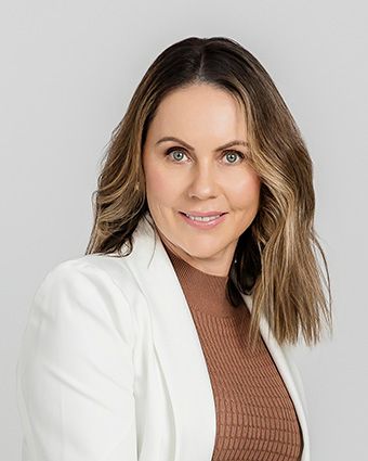 Professional real estate headshot of woman in a white blazer and brown top against a light gray background