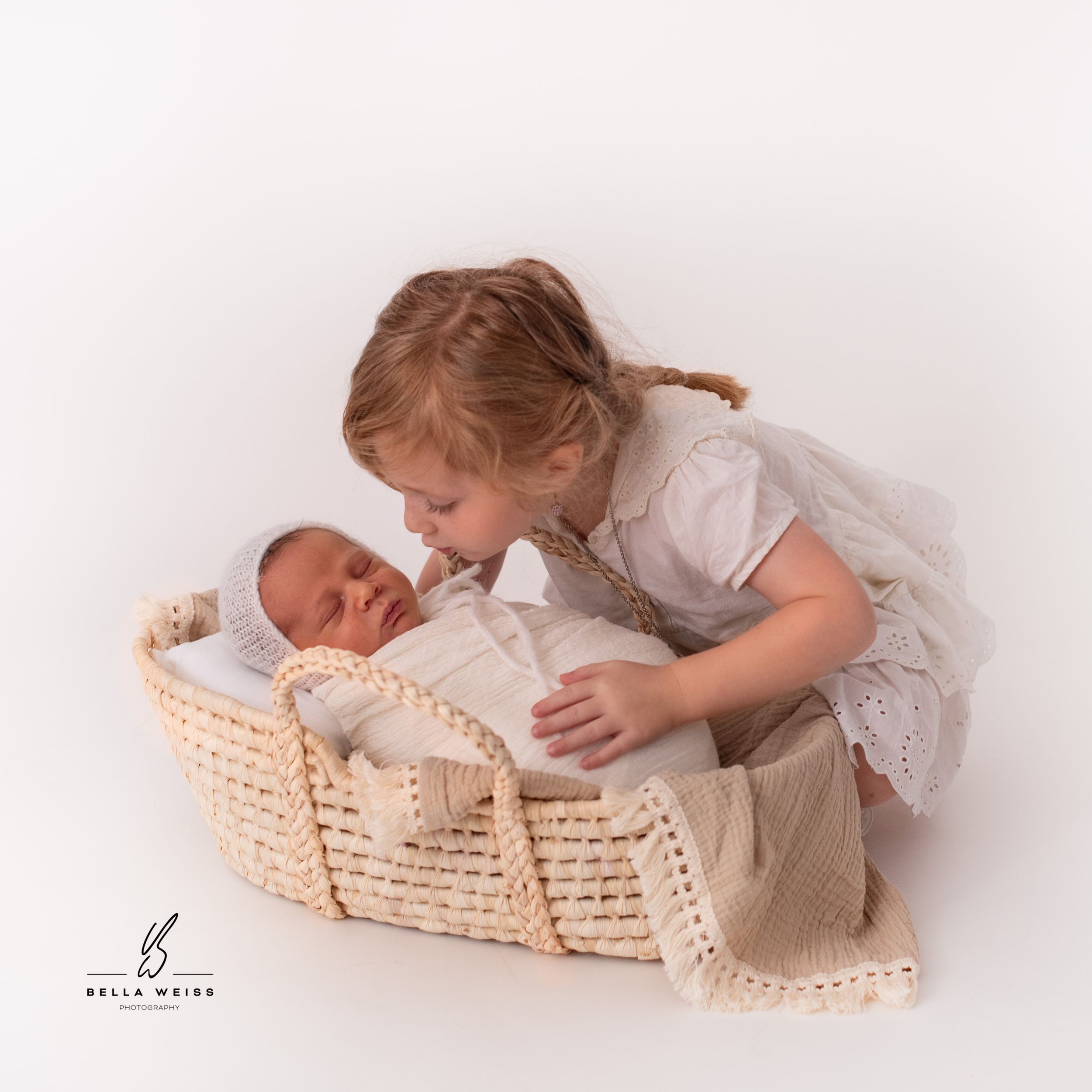 Sweet portrait of siblings with newborn baby in woven basket.