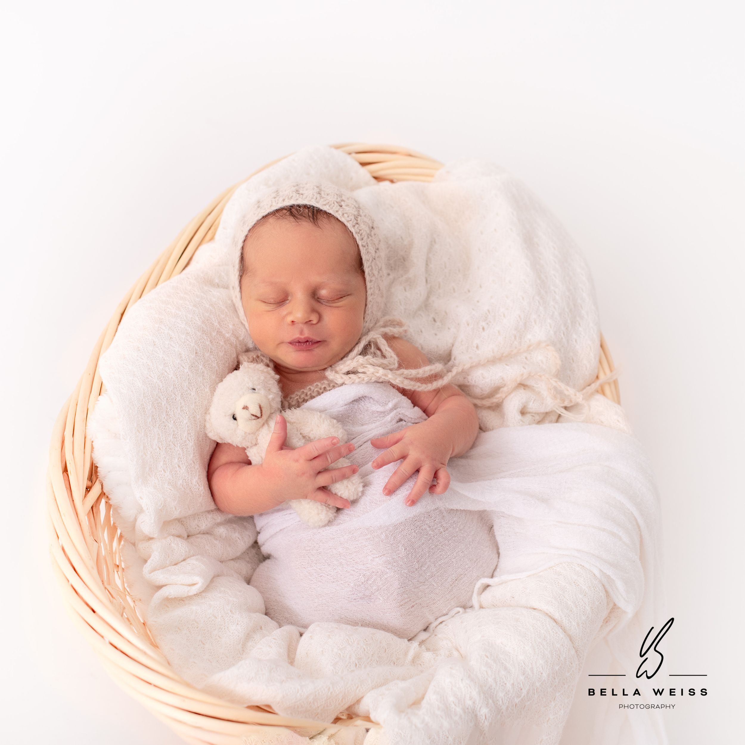 Peaceful sleeping newborn wrapped in white blanket in woven basket.