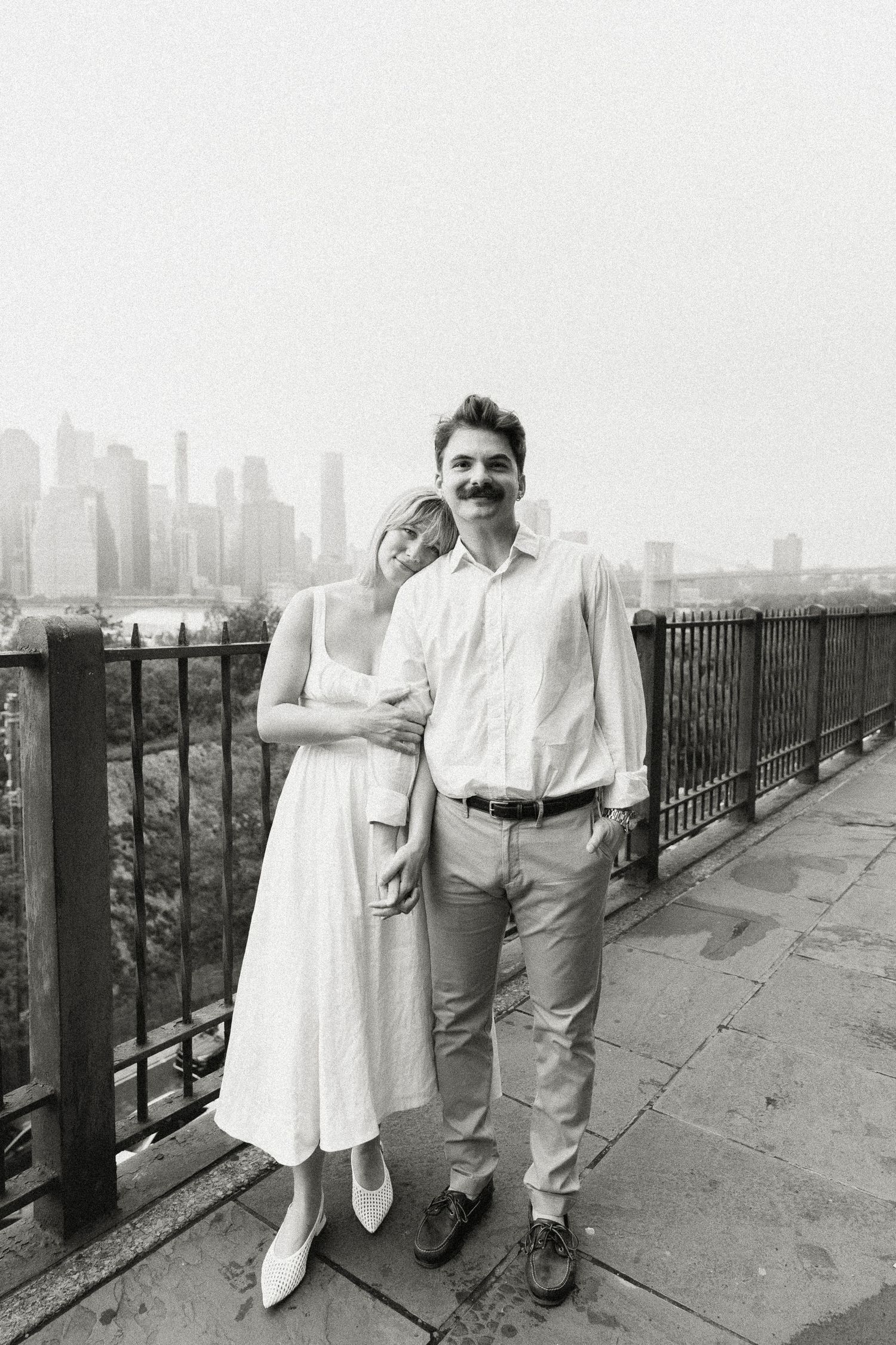 Black and white photo of a smiling engaged couple posing with NYC skyline behind them. Brooklyn Ny. Miranda Photo & Co