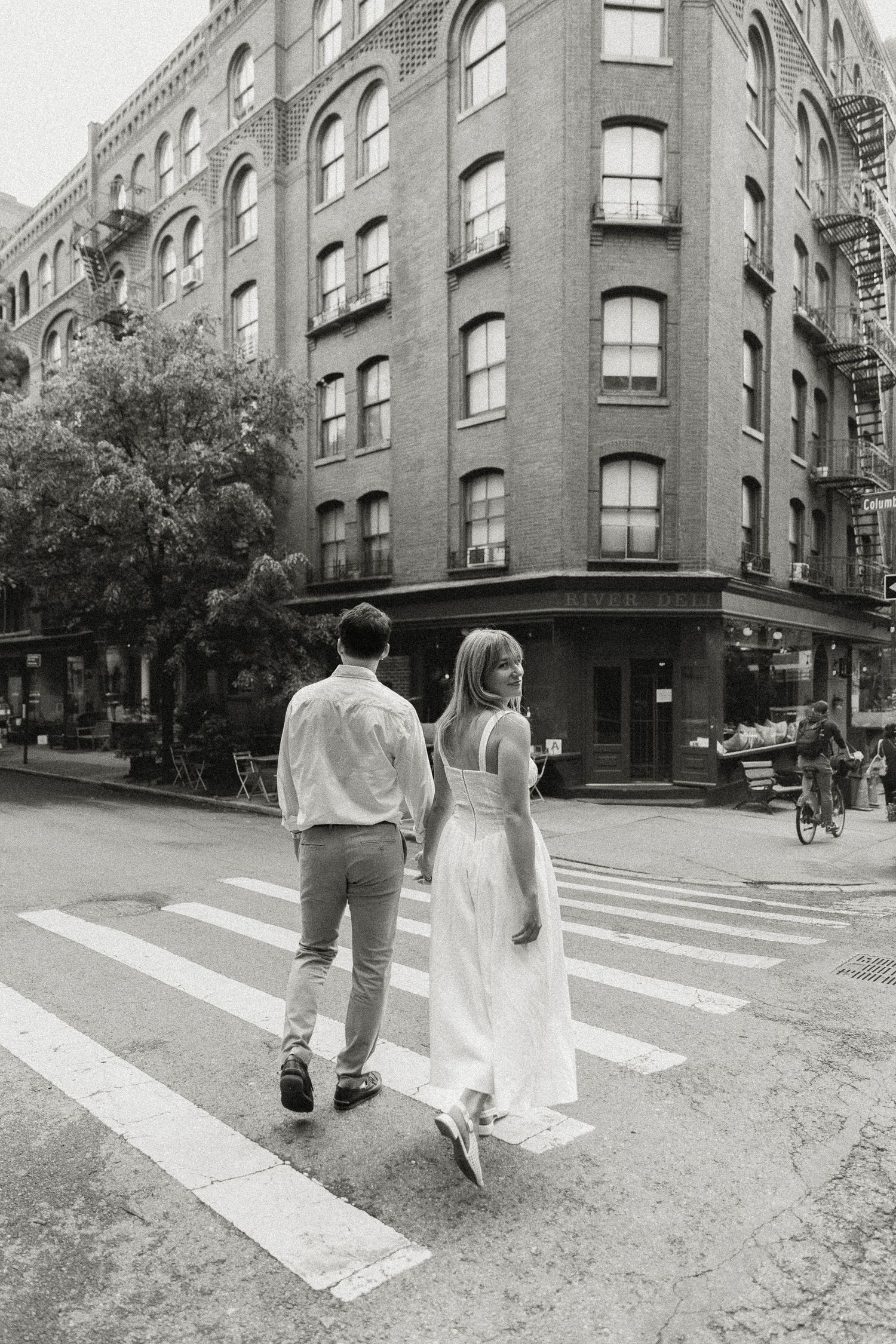 Black and white photo of a engaged couple holding hands while crossing a street in Brooklyn, New York City. Miranda Photo & Co