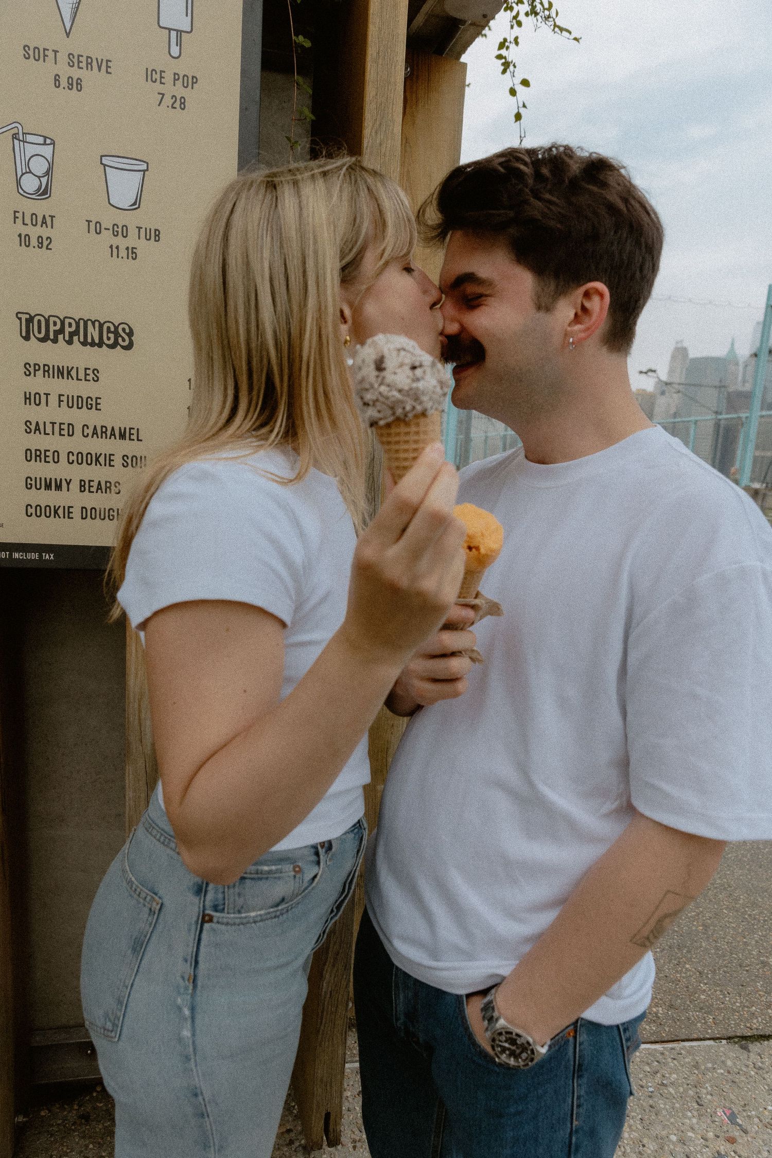 Engaged Couple sharing a playful kiss over ice cream cones outside a soft serve stand in the city. Brooklyn New York Miranda Photo & Co