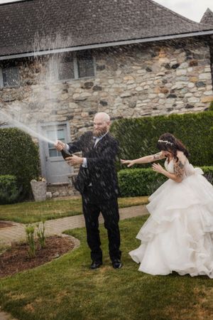 Groom pops the bottle of champagne and sprays bride.