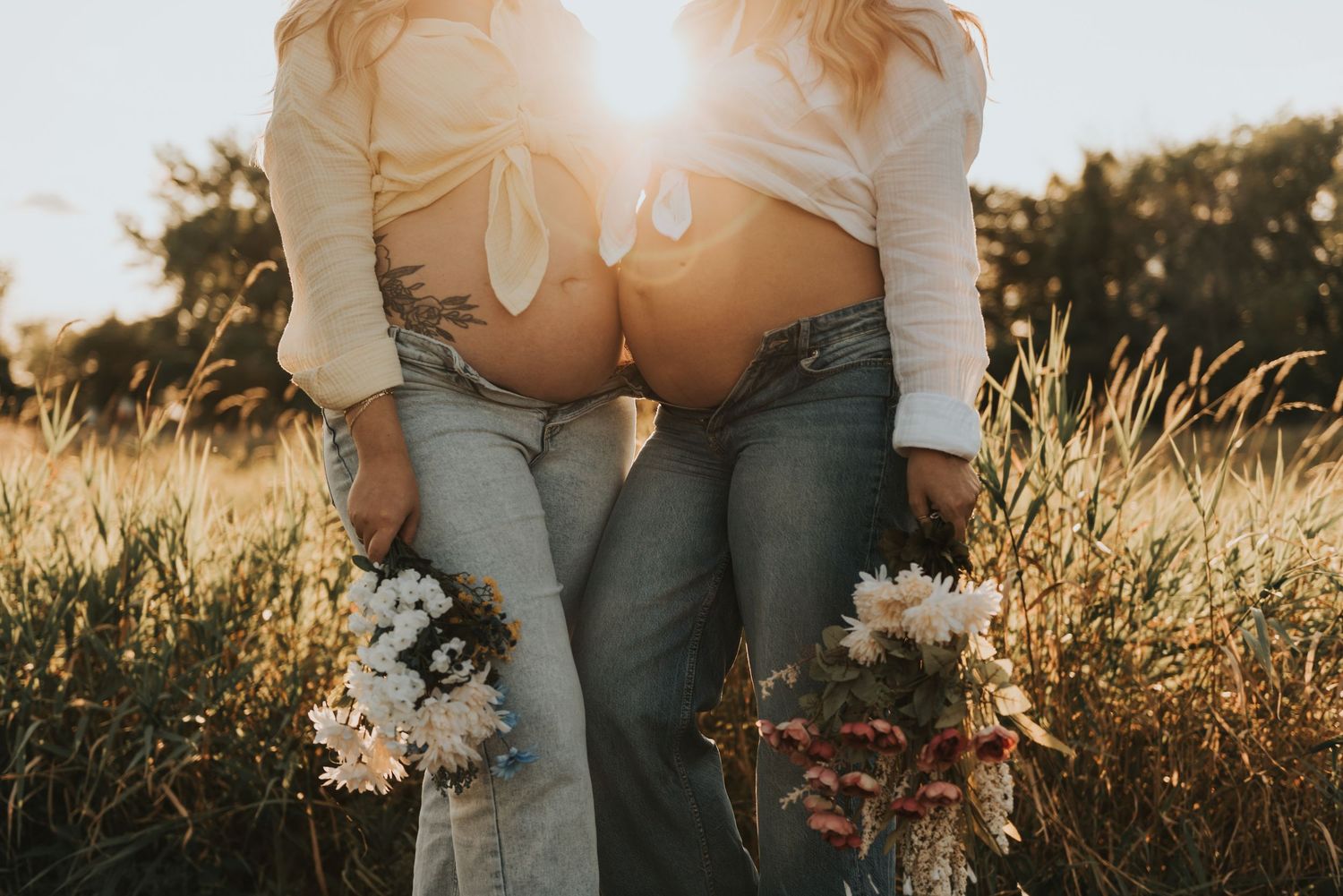 A couple sits together in a golden field during sunset while holding each other close.