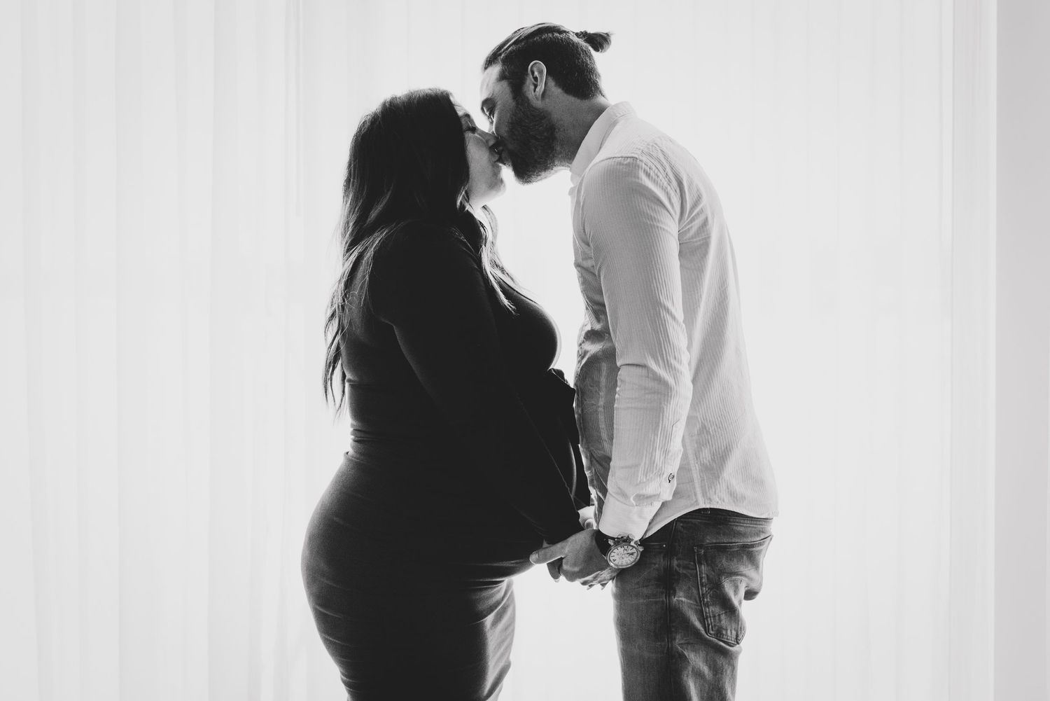 A silhouetted couple shares an intimate moment in black and white, with the woman showing a pregnant belly.