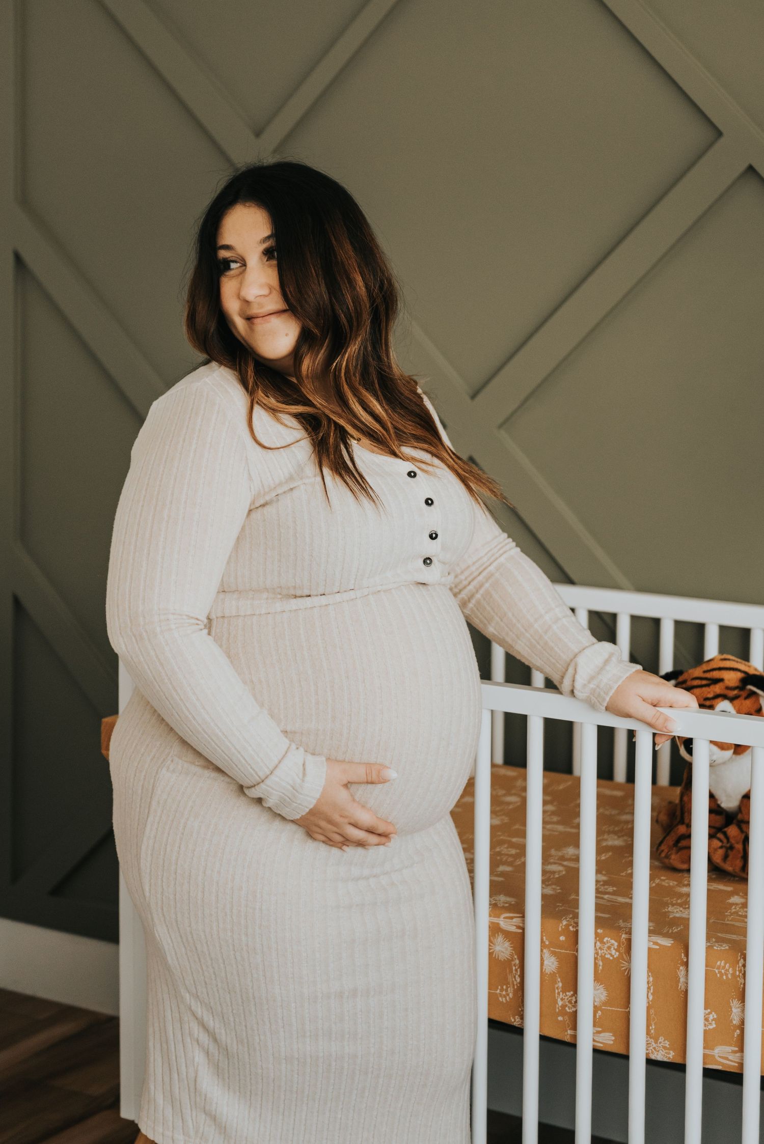 A person wearing a cozy white ribbed sweater poses against a gray lattice wall near white railing.