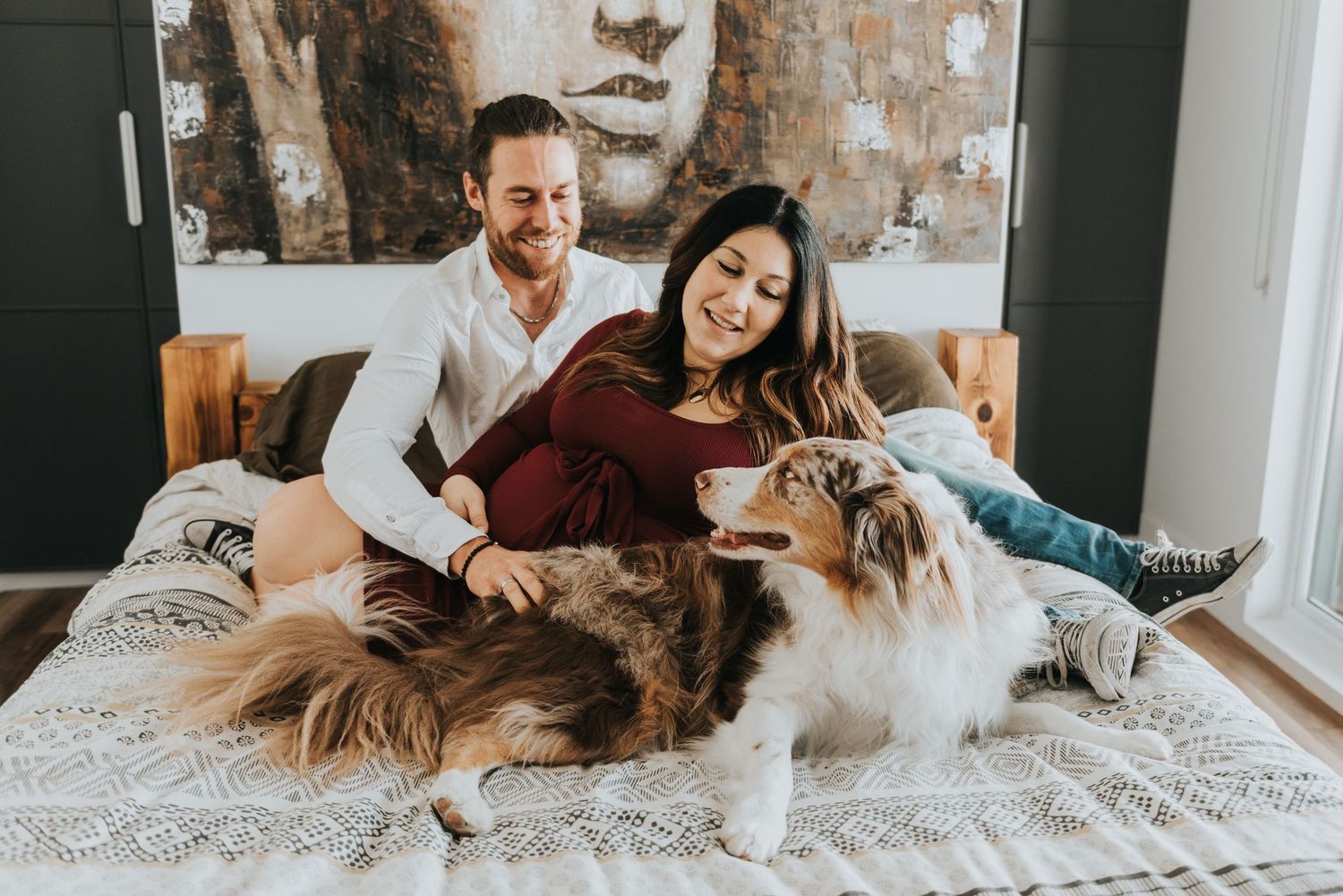 A couple and their dog relax together on a cozy white bed with textured bedding and exposed brick walls.