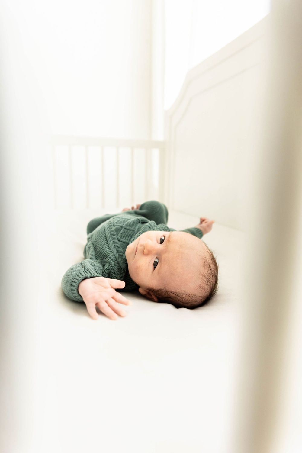 A newborn baby laying in a white crib. Lifestyle Newborn style.