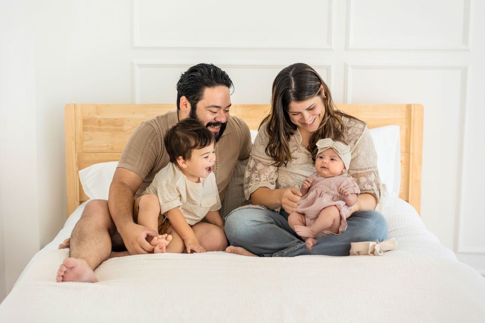 Family poses on a bed admiring new baby girl.