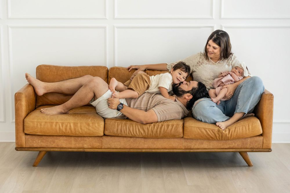 Family snuggles and laughs on a brown couch.