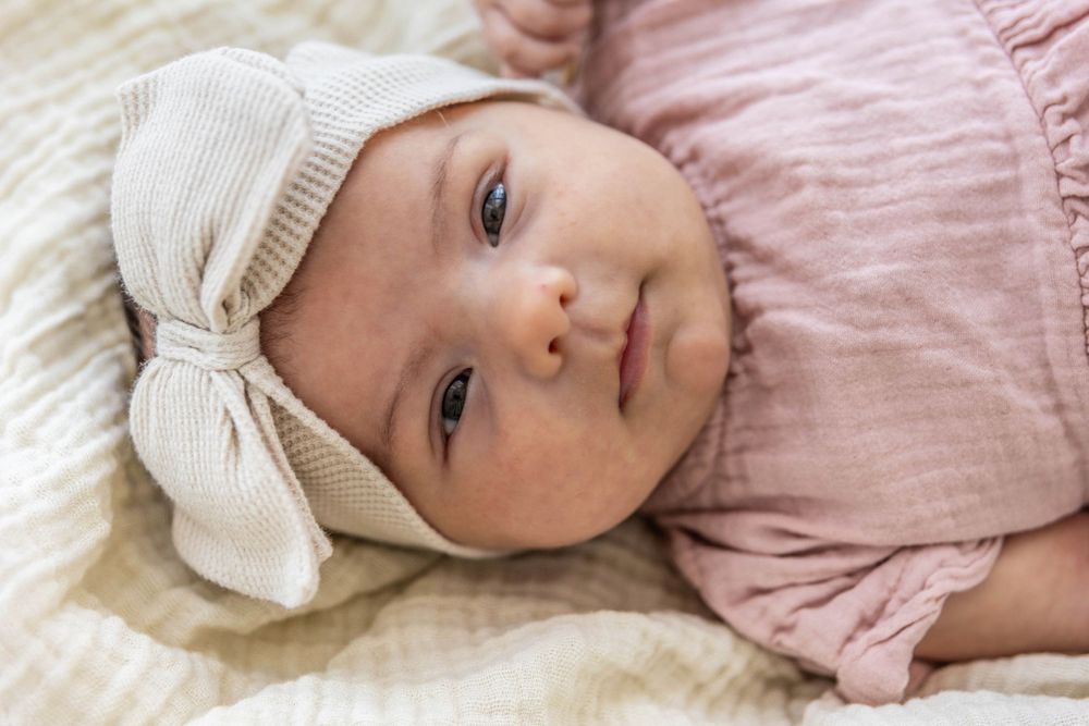 Close up of a baby girls face, white headband, pink dress.