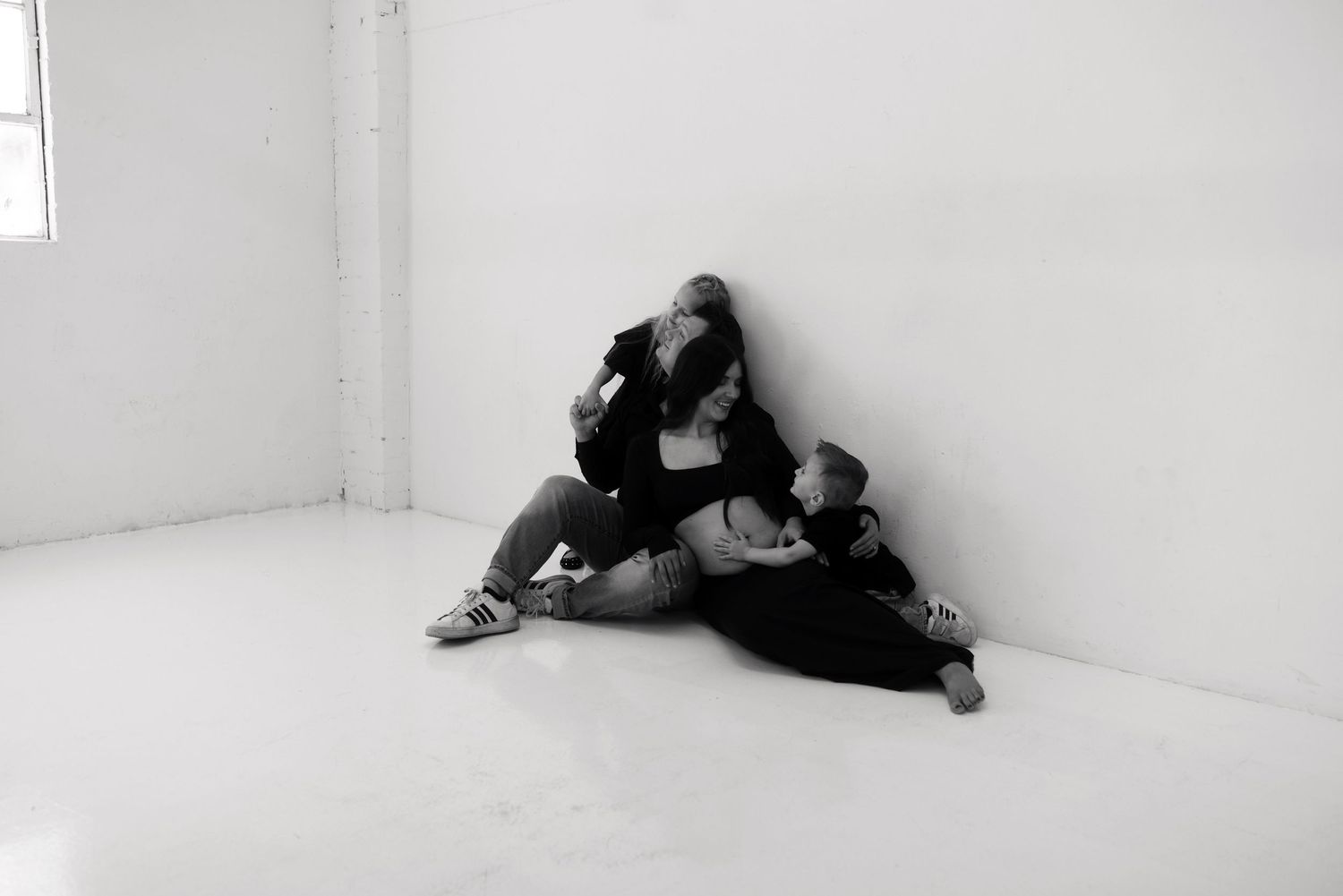 Black and white photo of a woman and children sitting together on a white studio floor against a wall.
