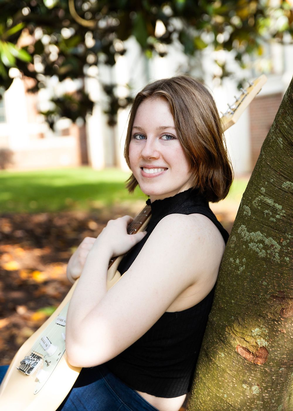 Portrait against tree in black sleeveless top with natural outdoor lighting.