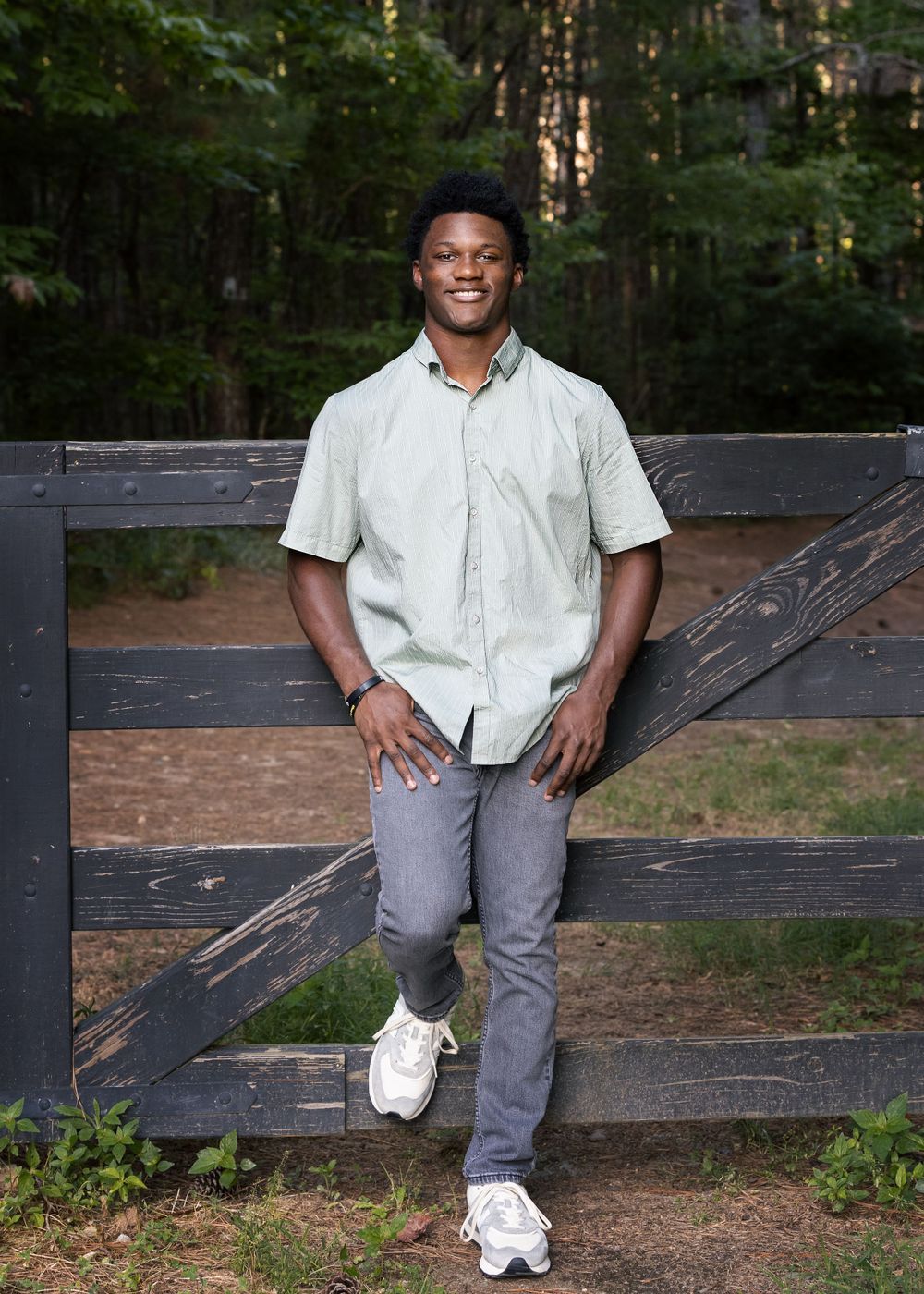 Portrait of person in casual white shirt leaning against wooden fence outdoors.