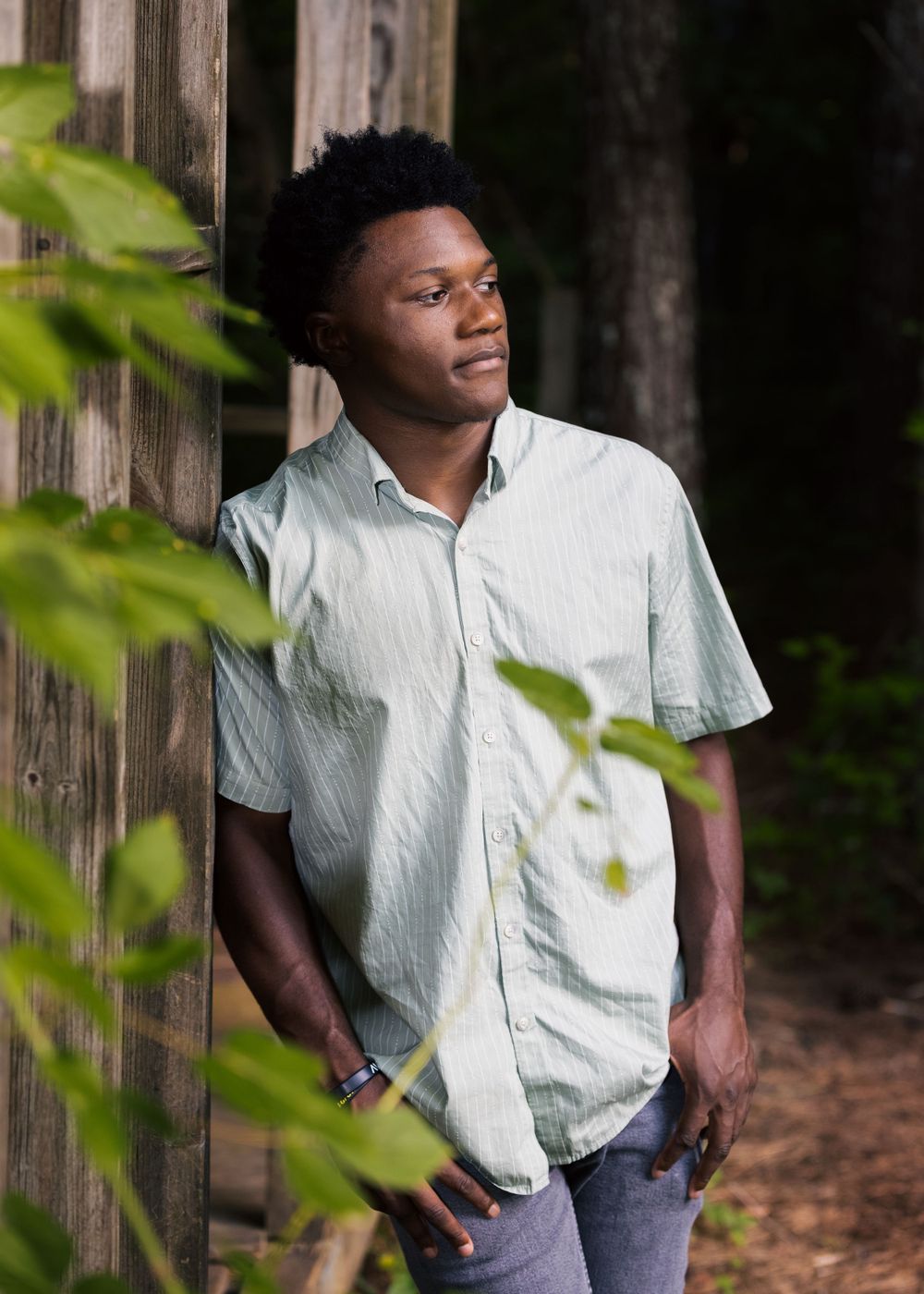 Portrait through leaves against wooden structure in natural lighting.
