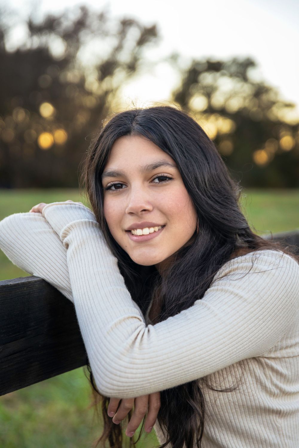 Portrait in white ribbed sweater leaning on fence during golden hour.