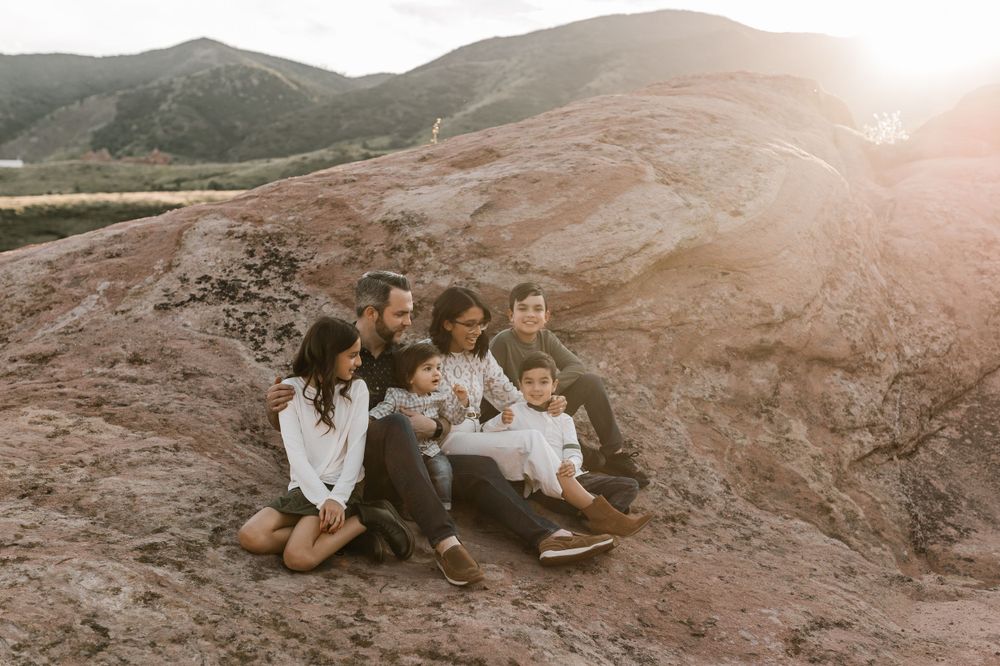 Family sitting together on red rocks during sunset in a desert landscape.