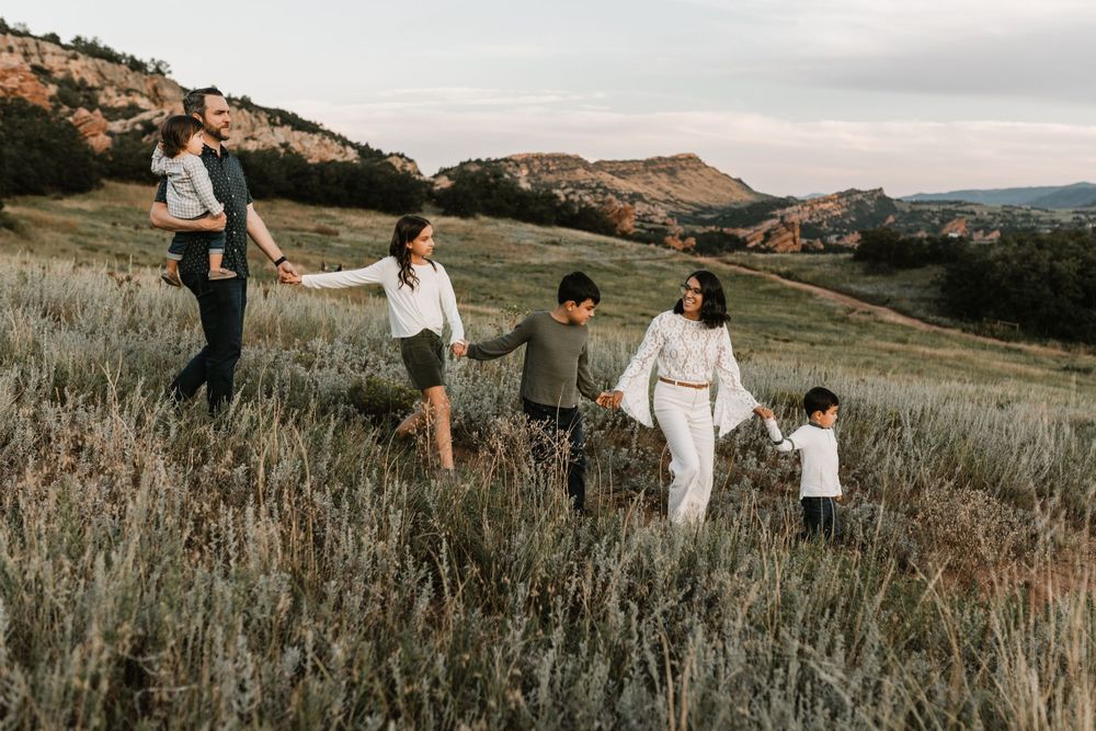 Family walking together through tall grass on a hillside during golden hour.