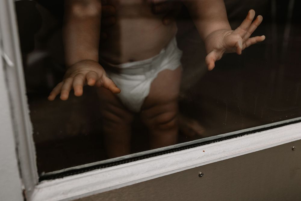 Small hands and feet of a baby in a diaper pressing against a glass window.