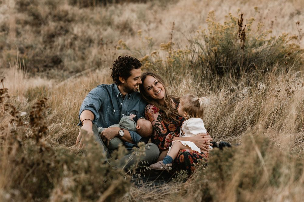 A family sitting together in tall grass with mountains visible in the distance.