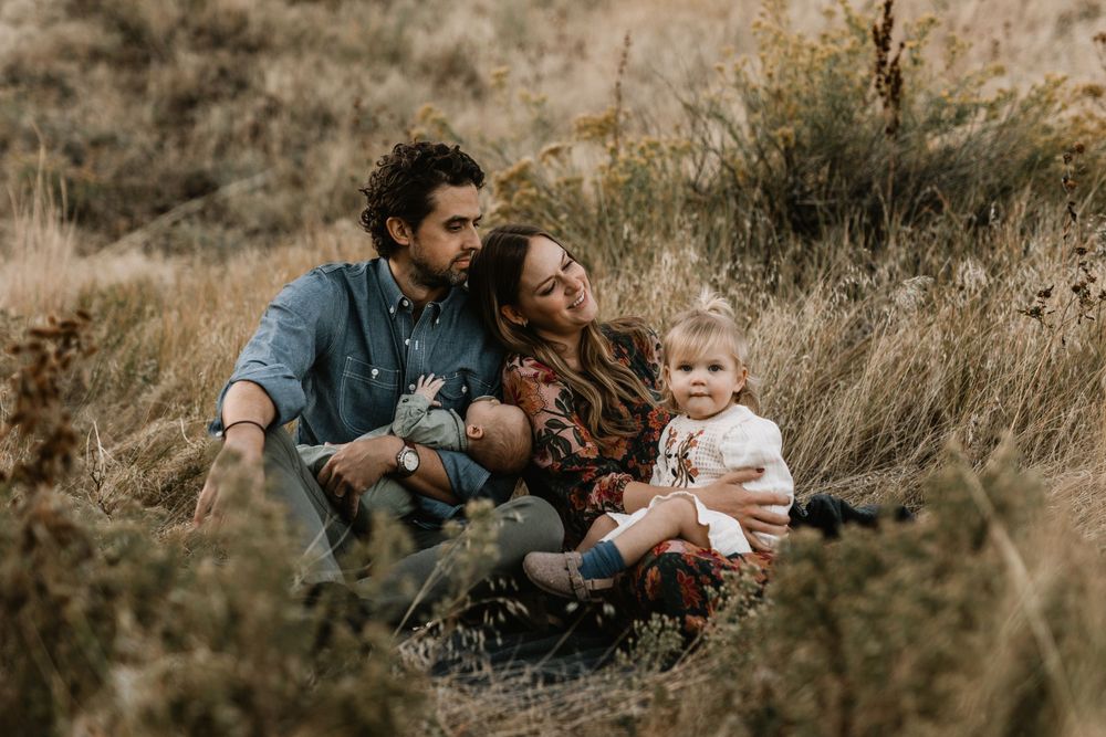 A family sits together in golden tall grass during sunset in a rustic outdoor setting.