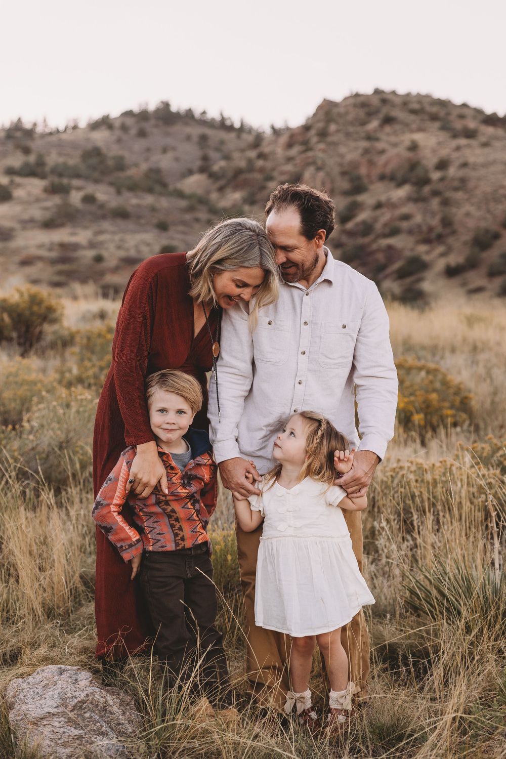 Family of four posing outdoors in a grassy field with mountain backdrop during golden hour family portrait session.