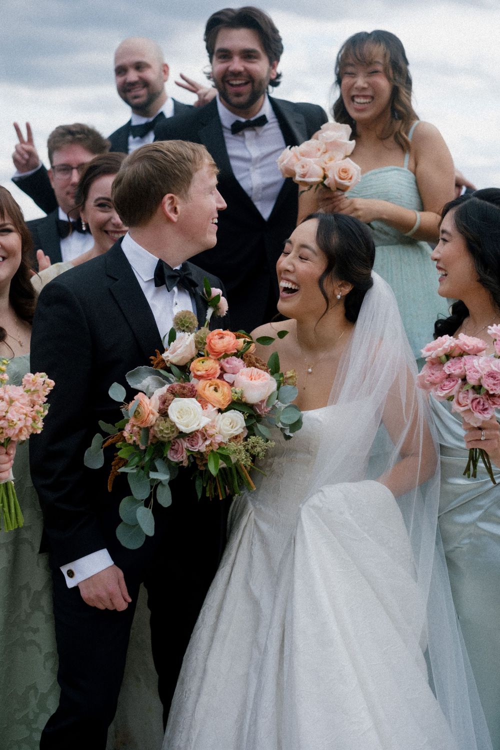A joyful wedding party celebrating outdoors with pink and peach floral bouquets.